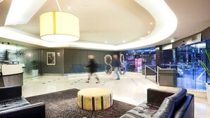 Eine moderne Lobby mit einer Rezeption, einer Sitzecke und großen Fenstern mit Blick auf die Straße.