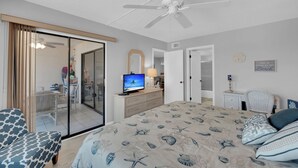 A bedroom with a bed, a TV, a ceiling fan, and a sliding glass door leading to a balcony. - 2B/2B Fairview Isles 222 Condo, Walk to Beach, Heated Pool! (Fort Myers Beach)