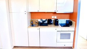 Una cucina compatta con mobili bianchi, un lavello, una macchina da caffè, un tostapane e un forno.