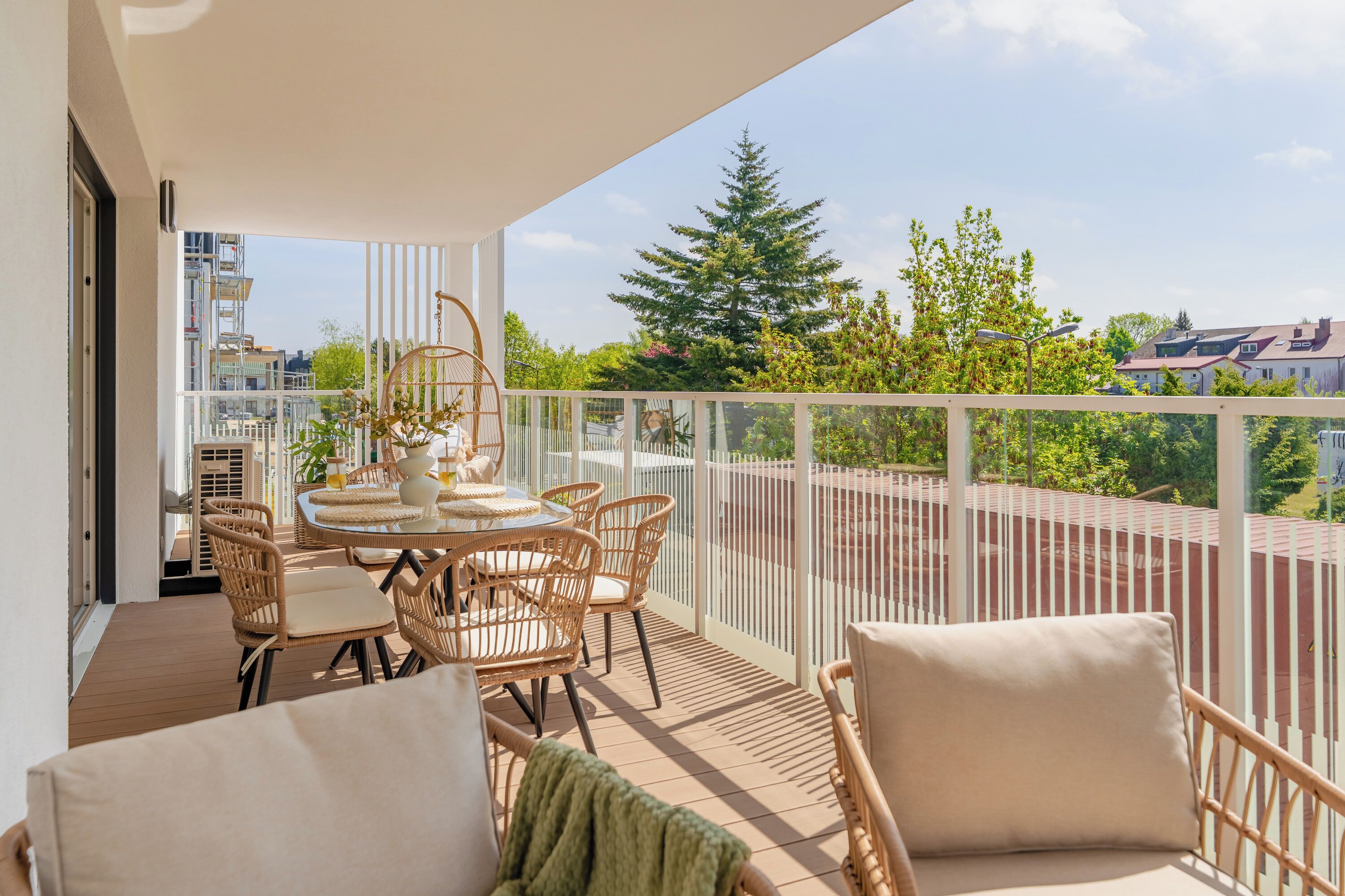 A balcony with wicker furniture, a round table, and a view of trees and buildings.