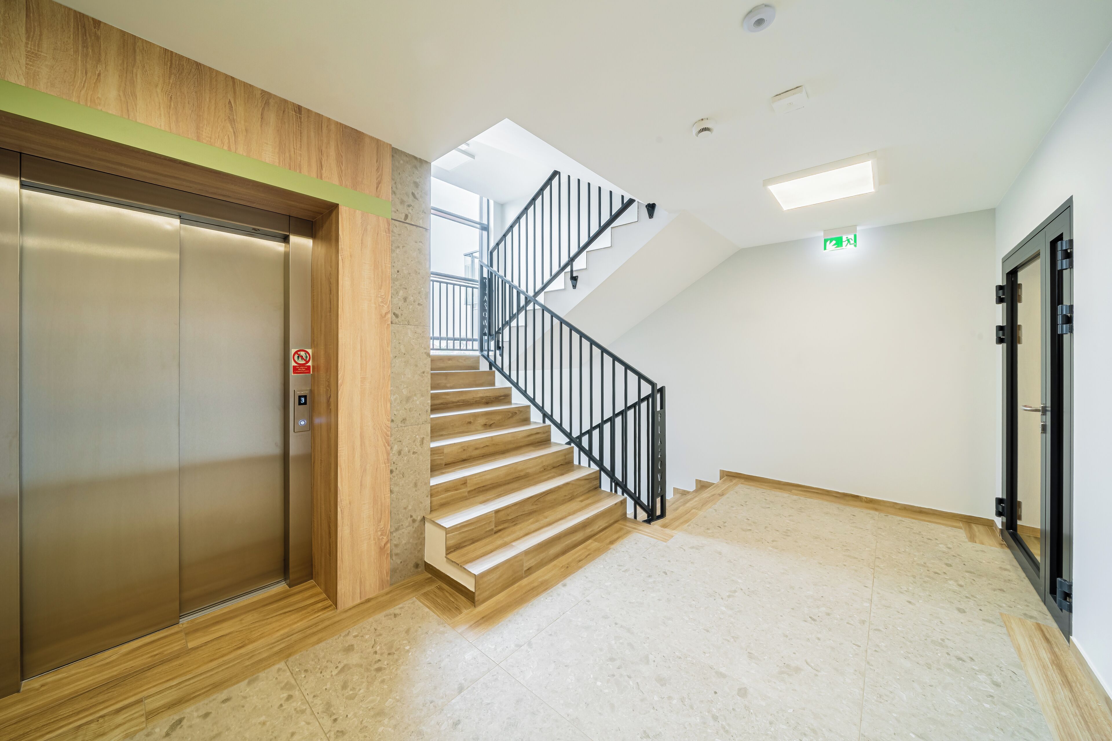 A modern elevator, a wooden staircase with a black railing, and a glass door.