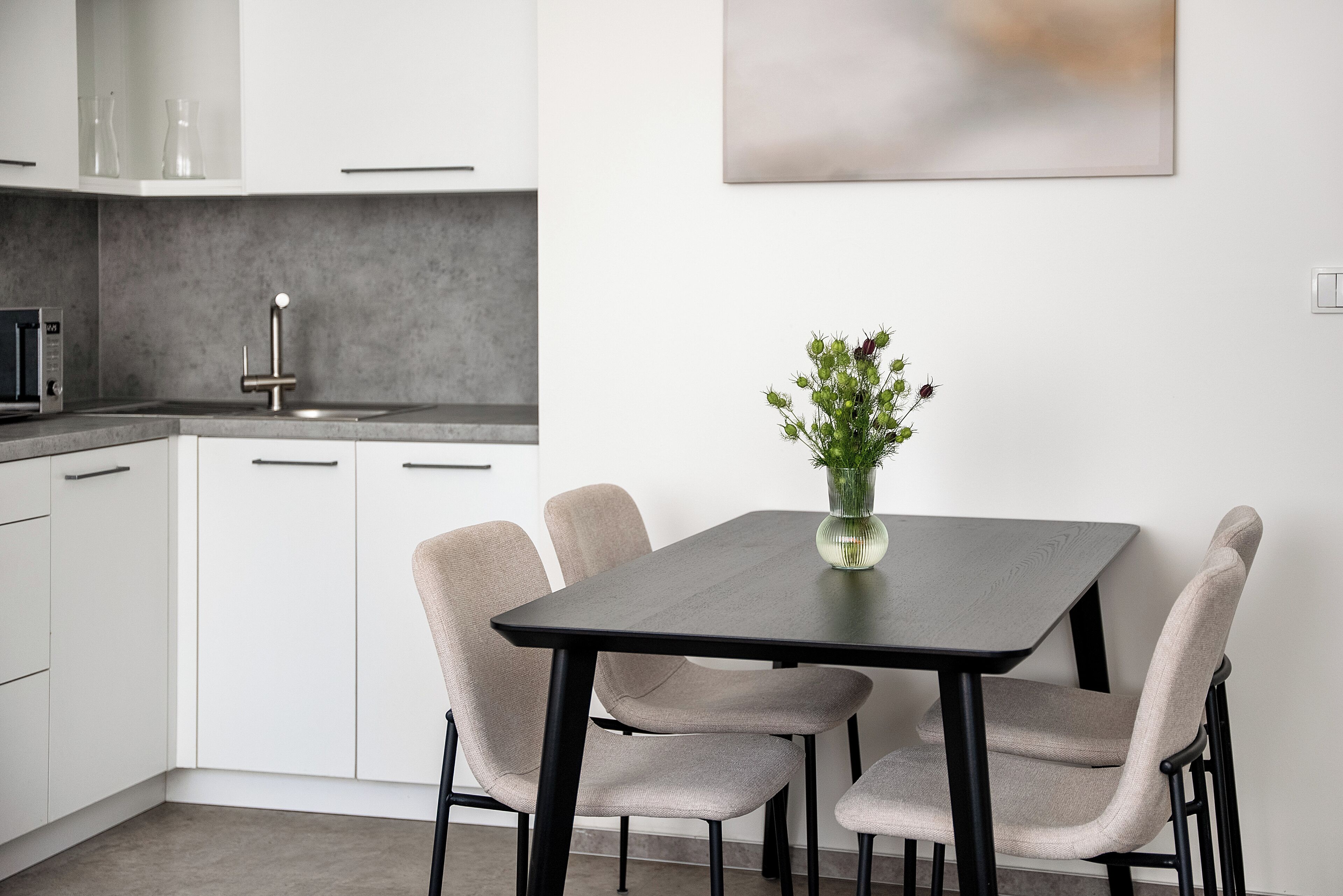 A modern kitchen with white cabinets, a dark countertop, and a vase with flowers on the table.