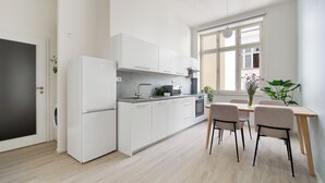Una cocina moderna con armarios blancos, una zona de comedor con mesa y sillas de madera, y un ventanal que proporciona luz natural.