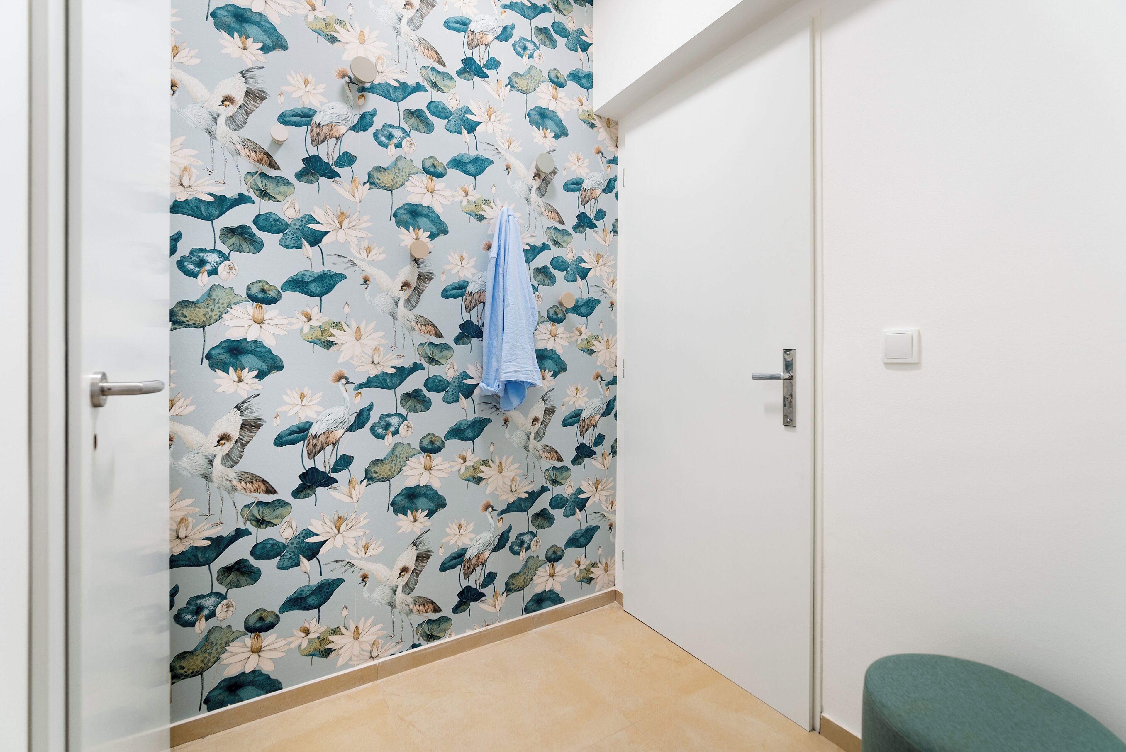 A bathroom with a floral wallpaper, a towel hanging on the wall, and a green bench.
