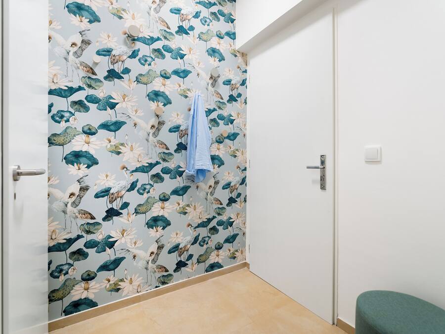 A bathroom with a floral wallpaper, a towel hanging on the wall, and a green bench.