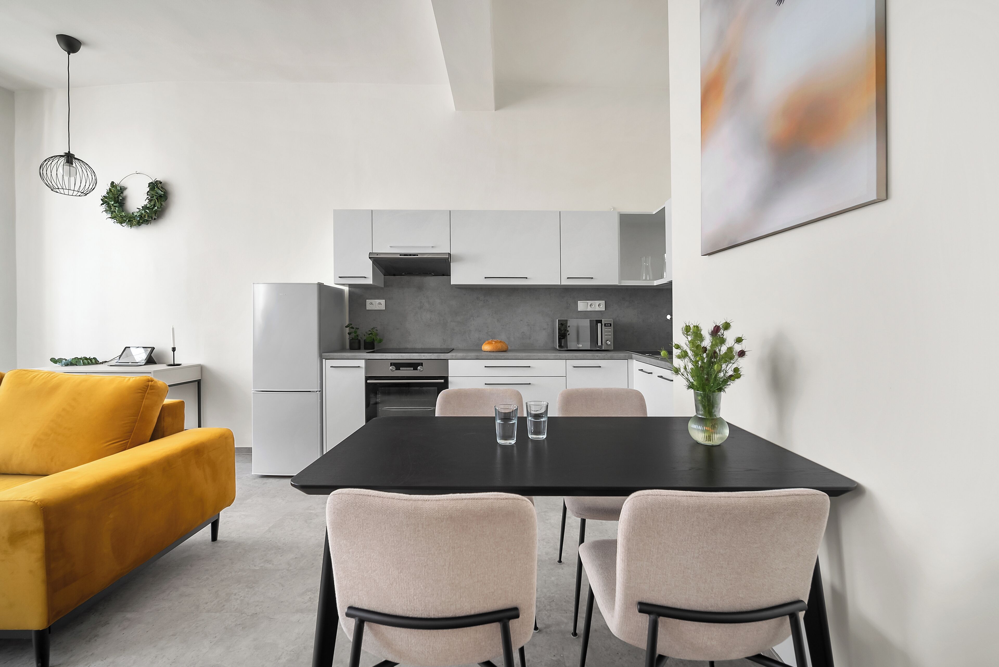 A modern kitchen with white cabinets, a black dining table, and a yellow sofa.