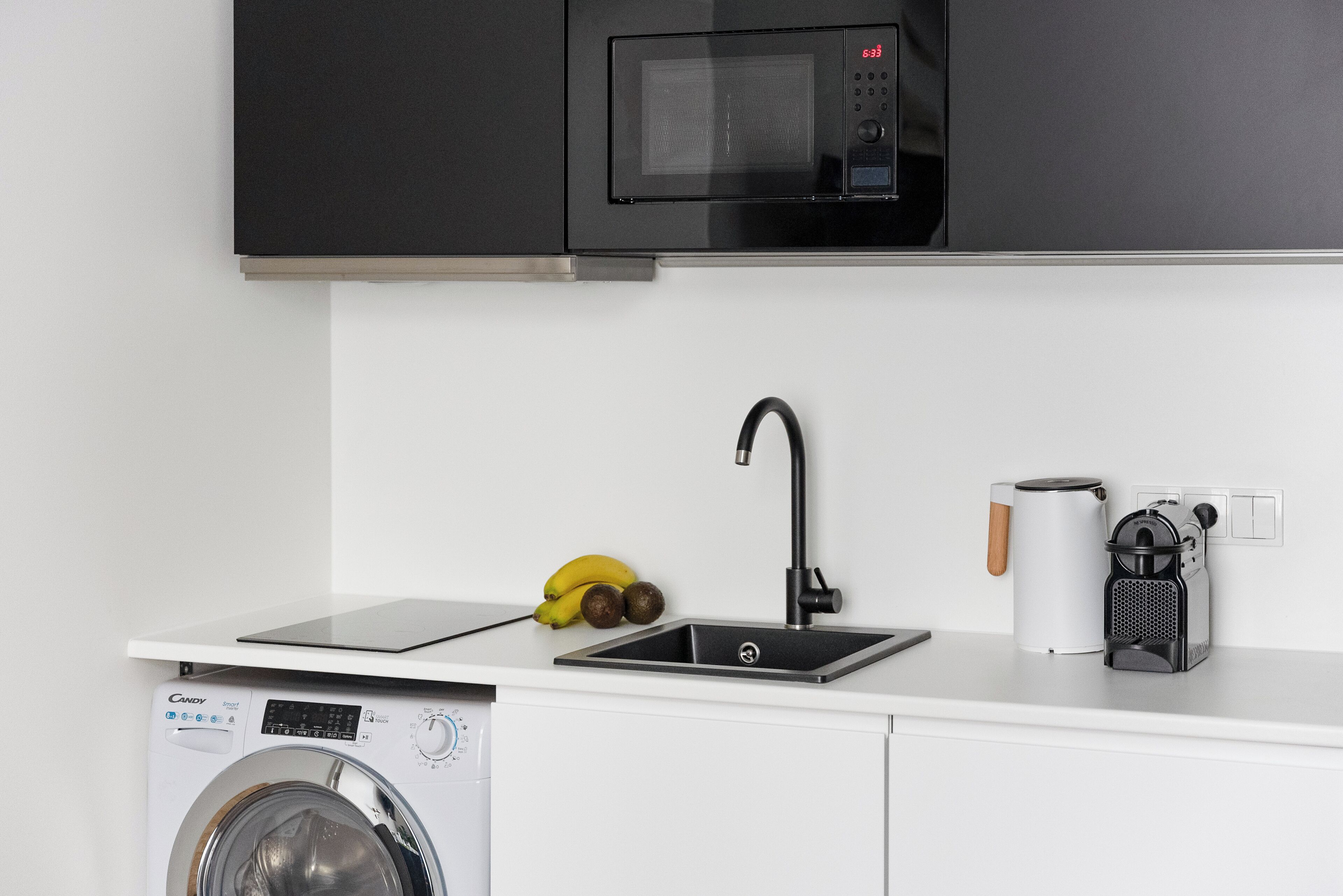 Una cocina equipada con lavadora, microondas, pileta y cafetera.
