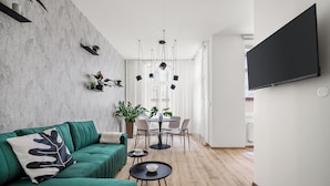 Una sala de estar moderna con un sofá verde, una mesa de comedor con sillas y un televisor montado en la pared.