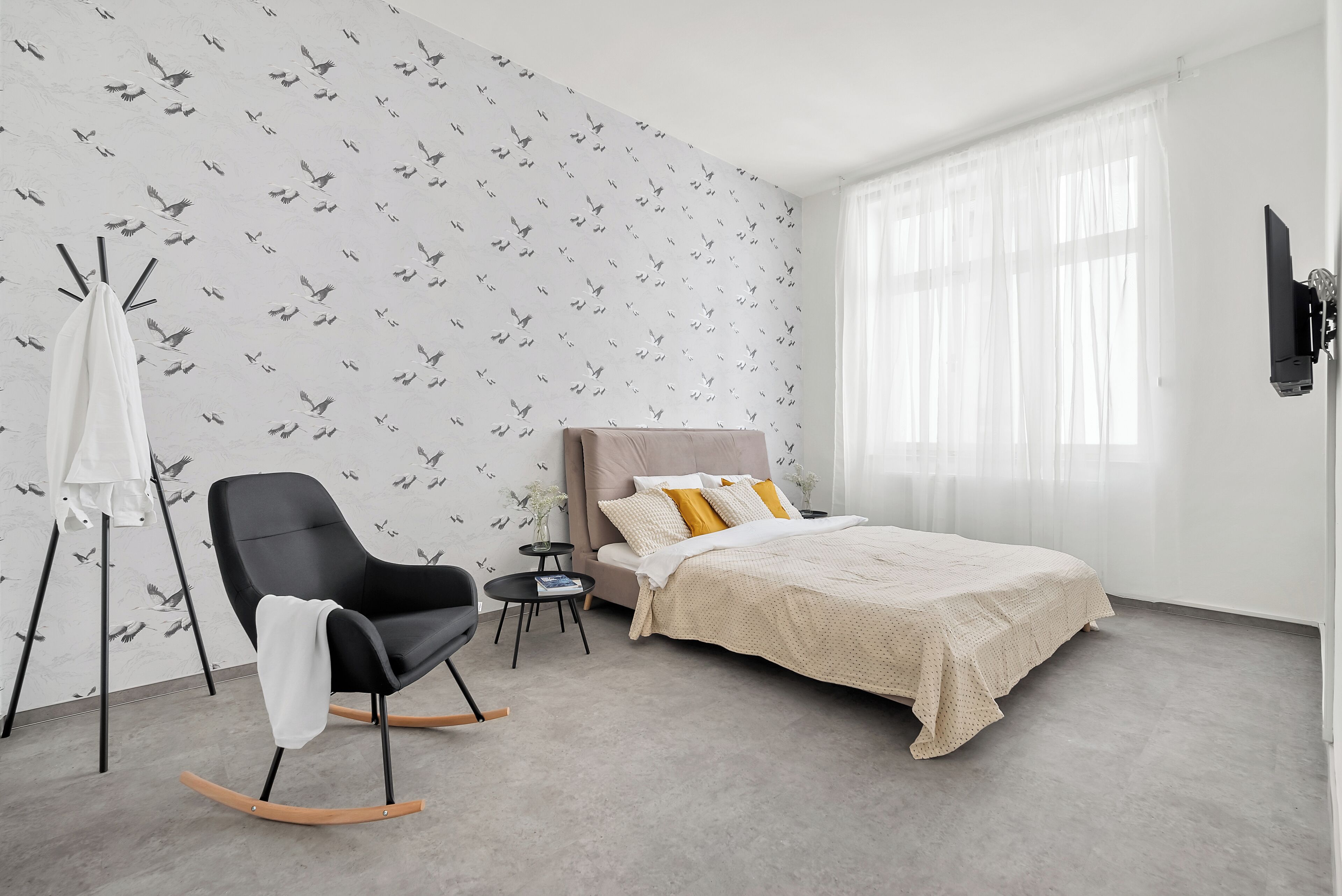 Een slaapkamer met een bed, een schommelstoel, een klein tafeltje en een tv aan de muur.