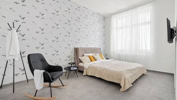 Een slaapkamer met een bed, een schommelstoel, een klein tafeltje en een tv aan de muur.