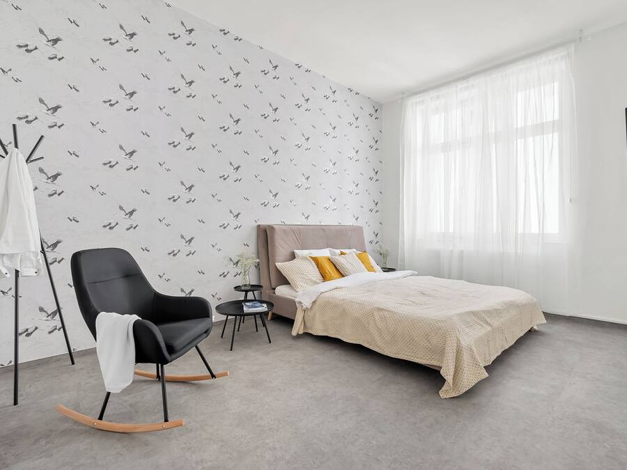 Een slaapkamer met een bed, een schommelstoel, een klein tafeltje en een tv aan de muur.