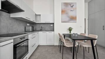 A modern kitchen with white cabinetry, a black countertop, and a dining area with a black table and beige chairs.
