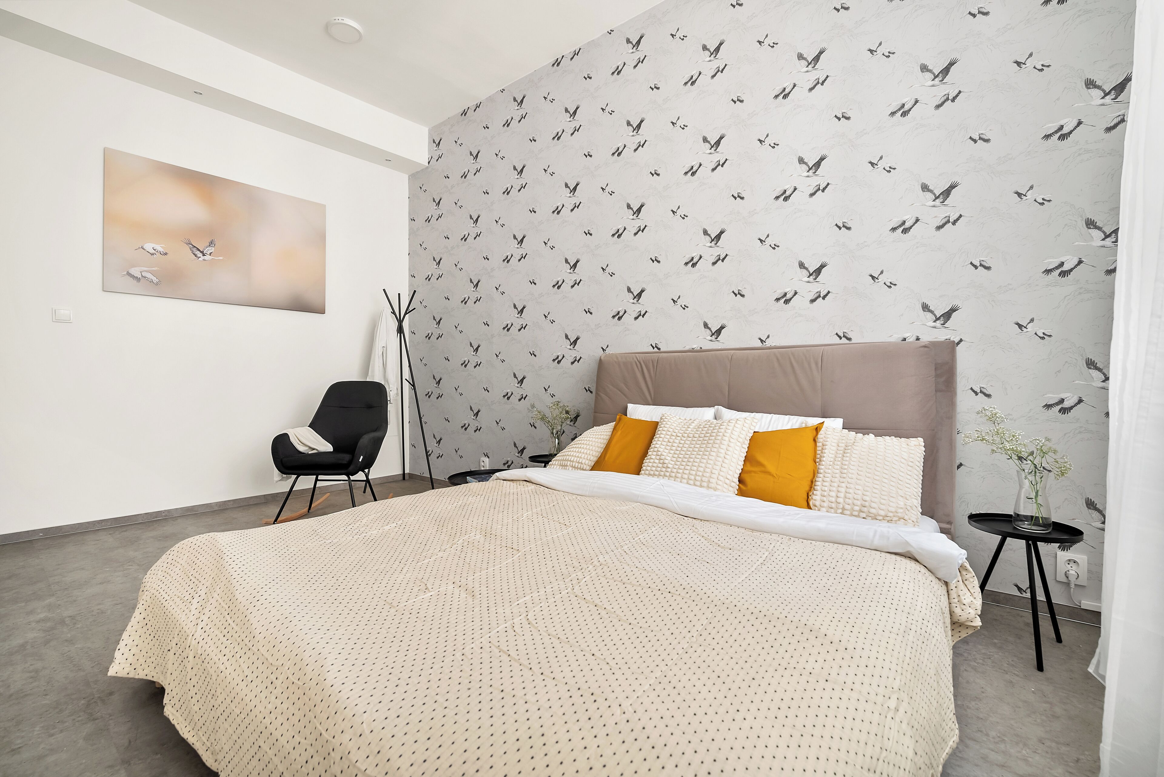 A bedroom with a bed, a chair, a small table, and a wall with a bird pattern.