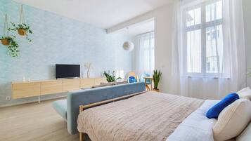 A modern bedroom with a bed, a TV, a wooden dresser, and a large window.