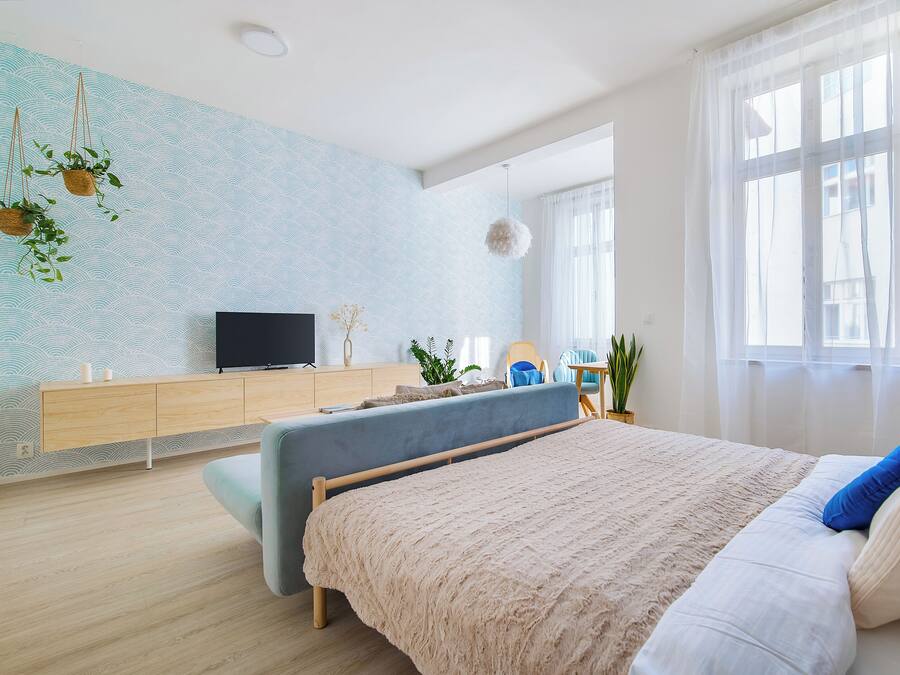 A modern bedroom with a bed, a TV, a wooden dresser, and a large window.