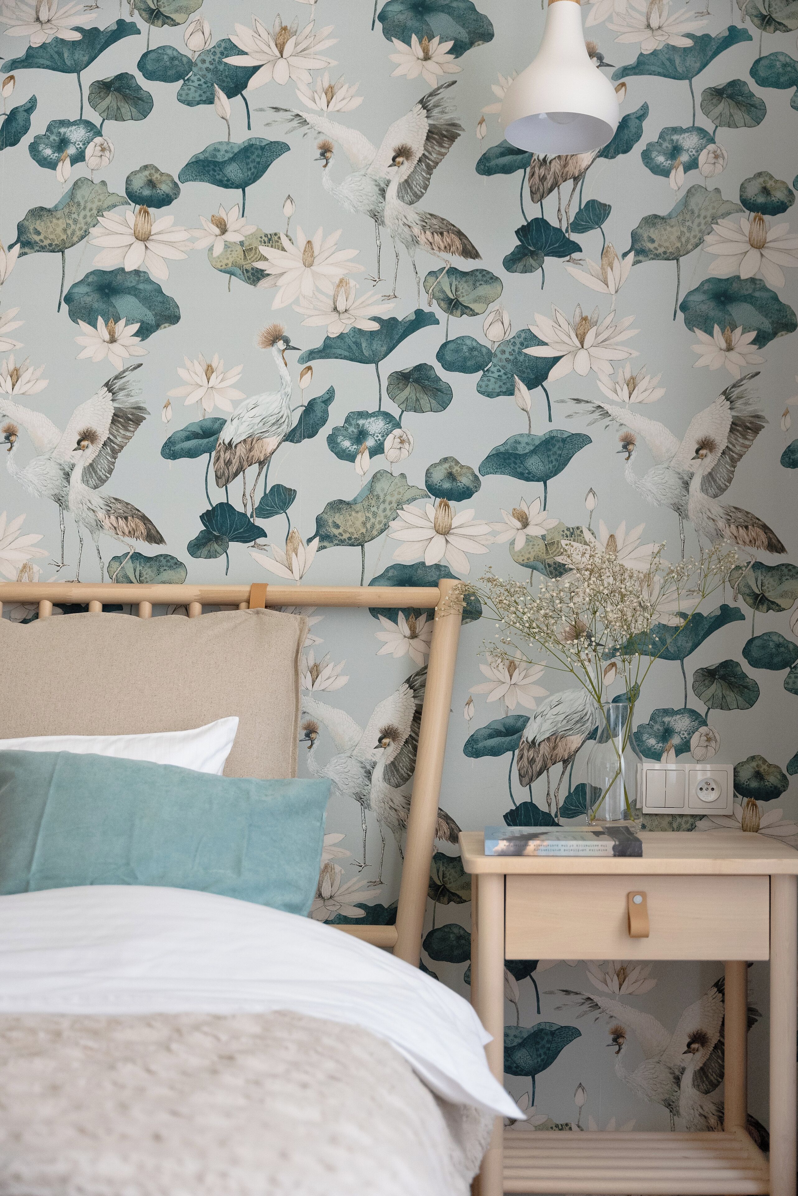 A bedroom with a bed, a nightstand with a lamp, and a wall with floral wallpaper.