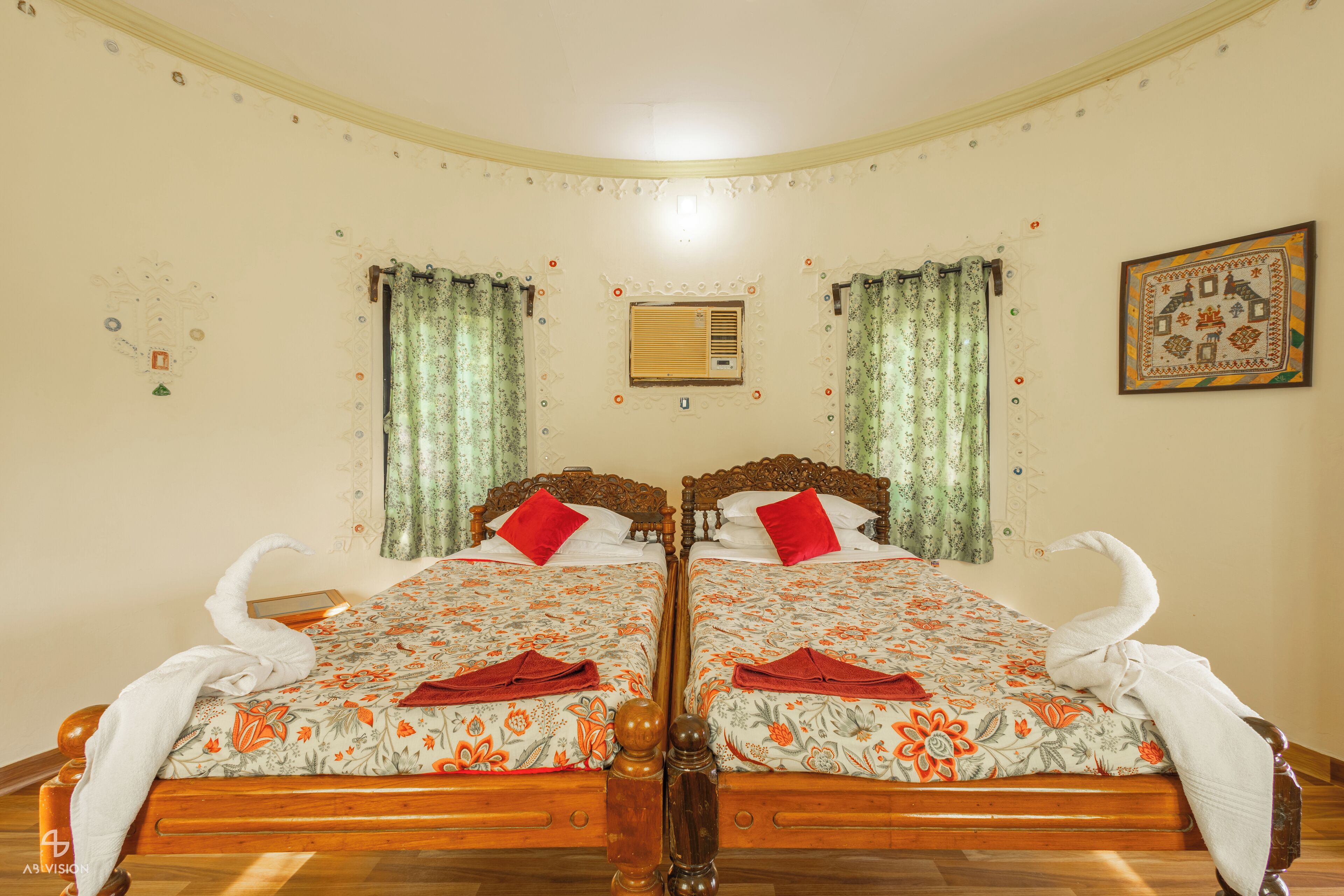 Una cama doble con ropa de cama floral, dos almohadas rojas y toallas con forma de cisnes.