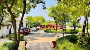 A paved driveway leading to a building with a red roof, surrounded by trees and greenery.