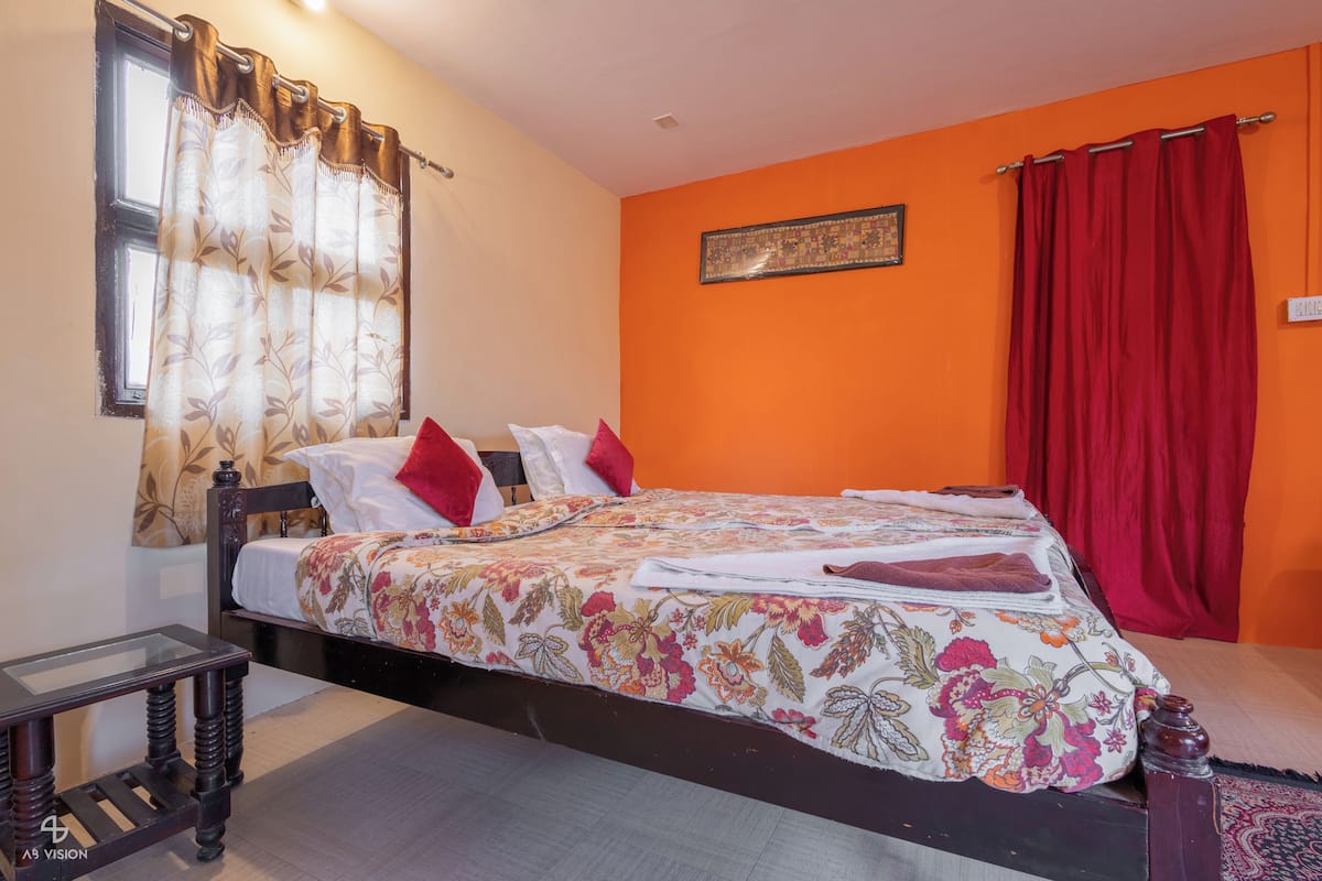 Une chambre à coucher avec un lit, une table de chevet, une fenêtre avec des rideaux et un mur orné d’un tableau.