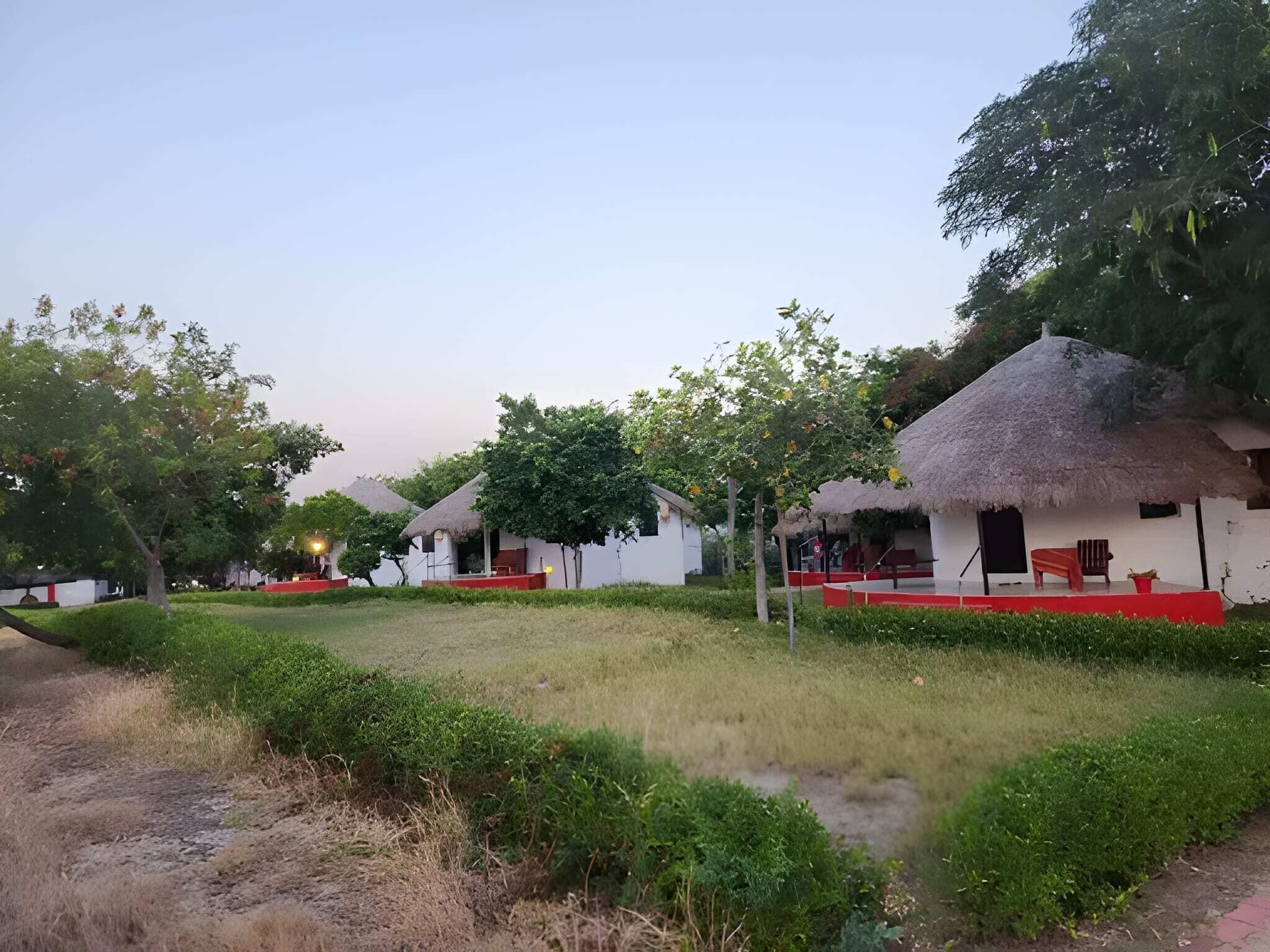 A rural village with thatched-roof houses, a grassy courtyard, and a clear sky.