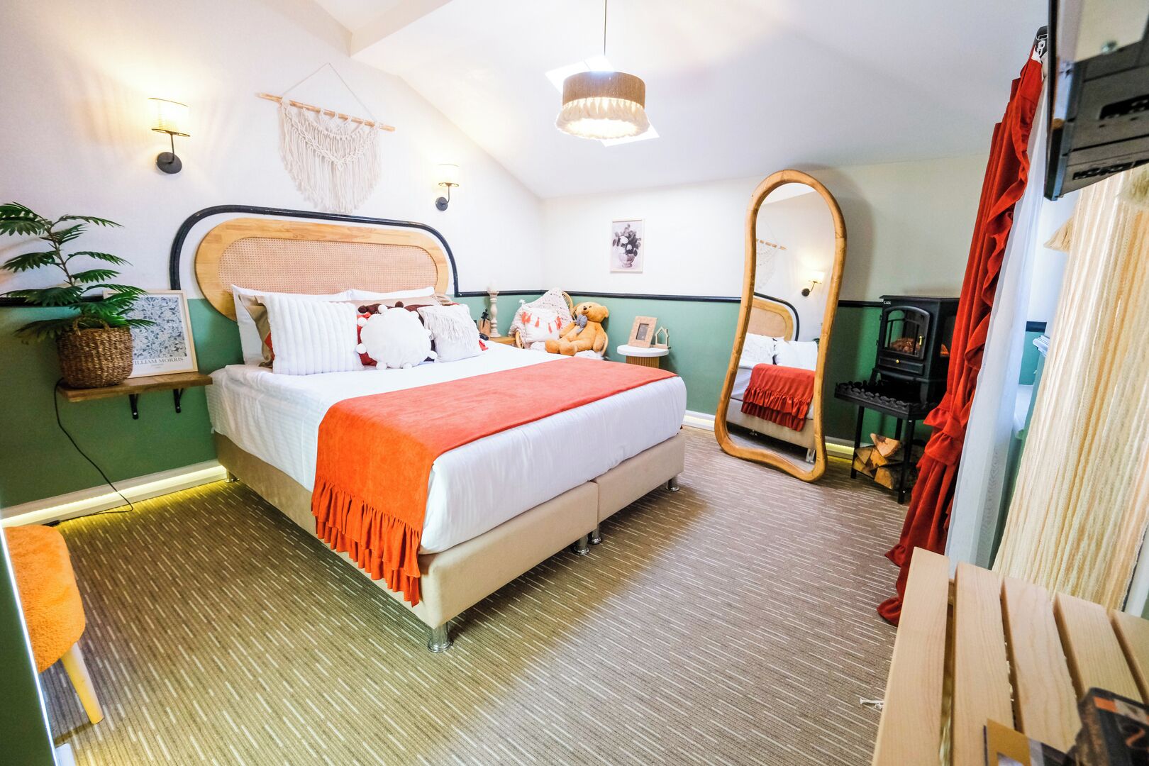A bedroom with a bed, bedside table, mirror, wall-mounted shelf, and a hanging plant.