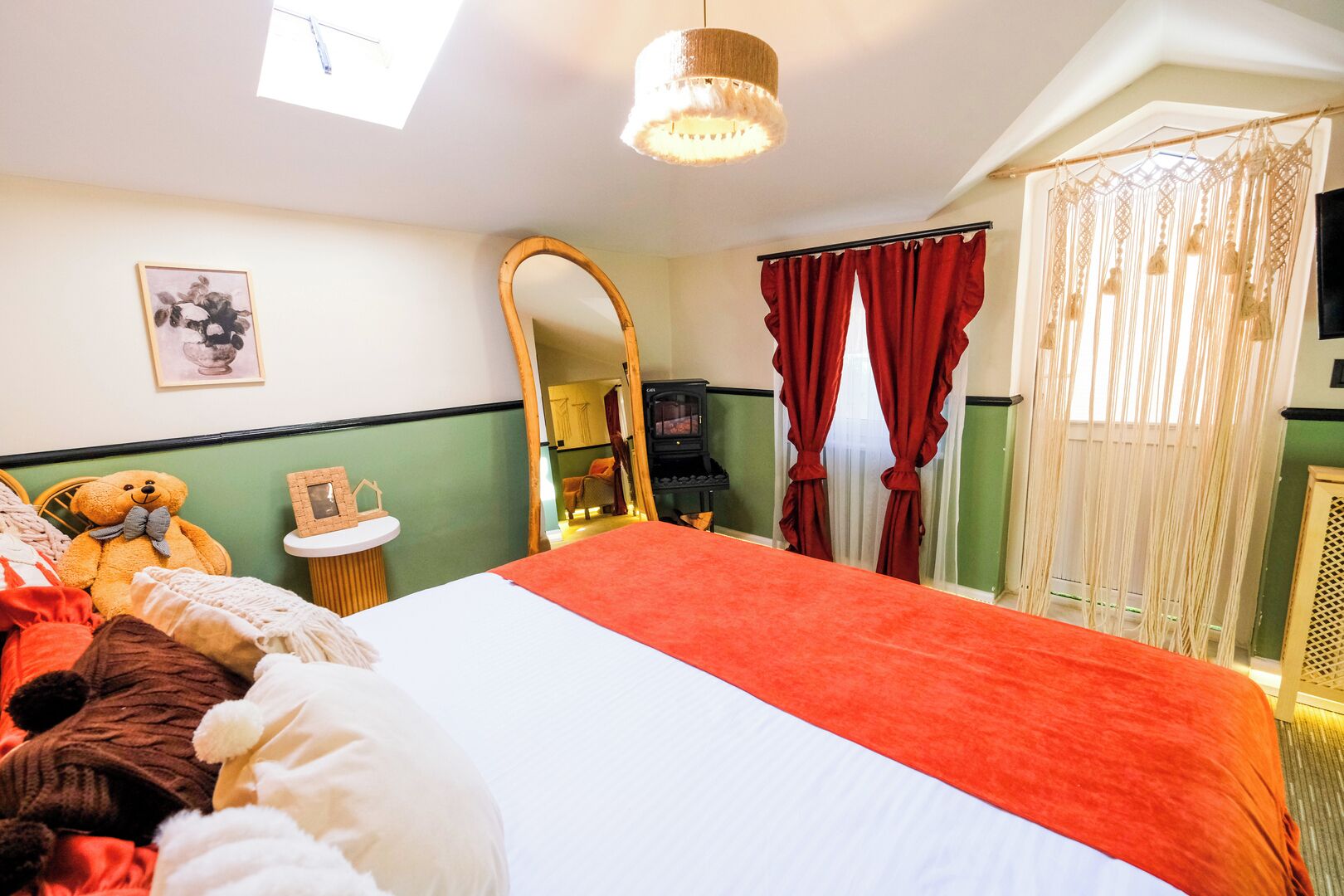 Un dormitorio con cama, un oso de peluche, un espejo, una mesita y una ventana con cortinas.