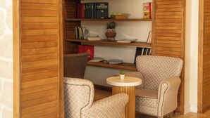 Eine gemütliche Leseecke mit einem Holzregal, zwei gemusterten Sesseln und einem kleinen runden Tisch.