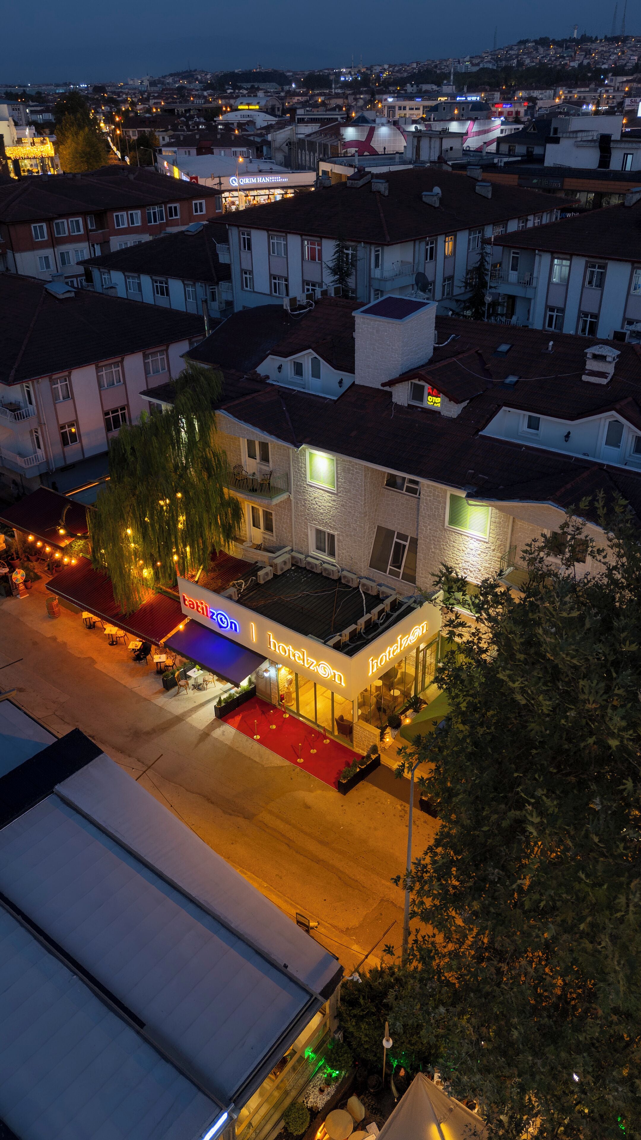 A hotel with a red carpet entrance, outdoor seating, and a sign reading "hotelzon".
