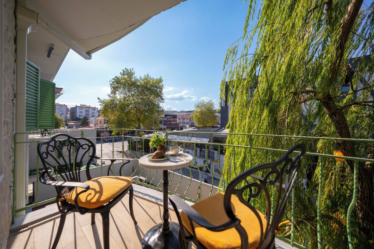 Ein Balkon mit zwei Stühlen und einem kleinen Tisch, der auf eine Stadtansicht mit Gebäuden und einem Fluss blickt.