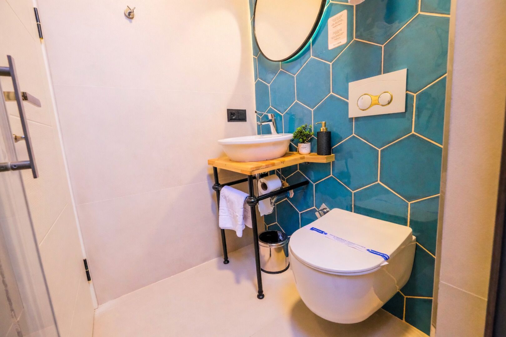 Un baño moderno con un inodoro blanco, un lavabo sobre un estante de madera, un espejo y un salpicadero de azulejos hexagonales.