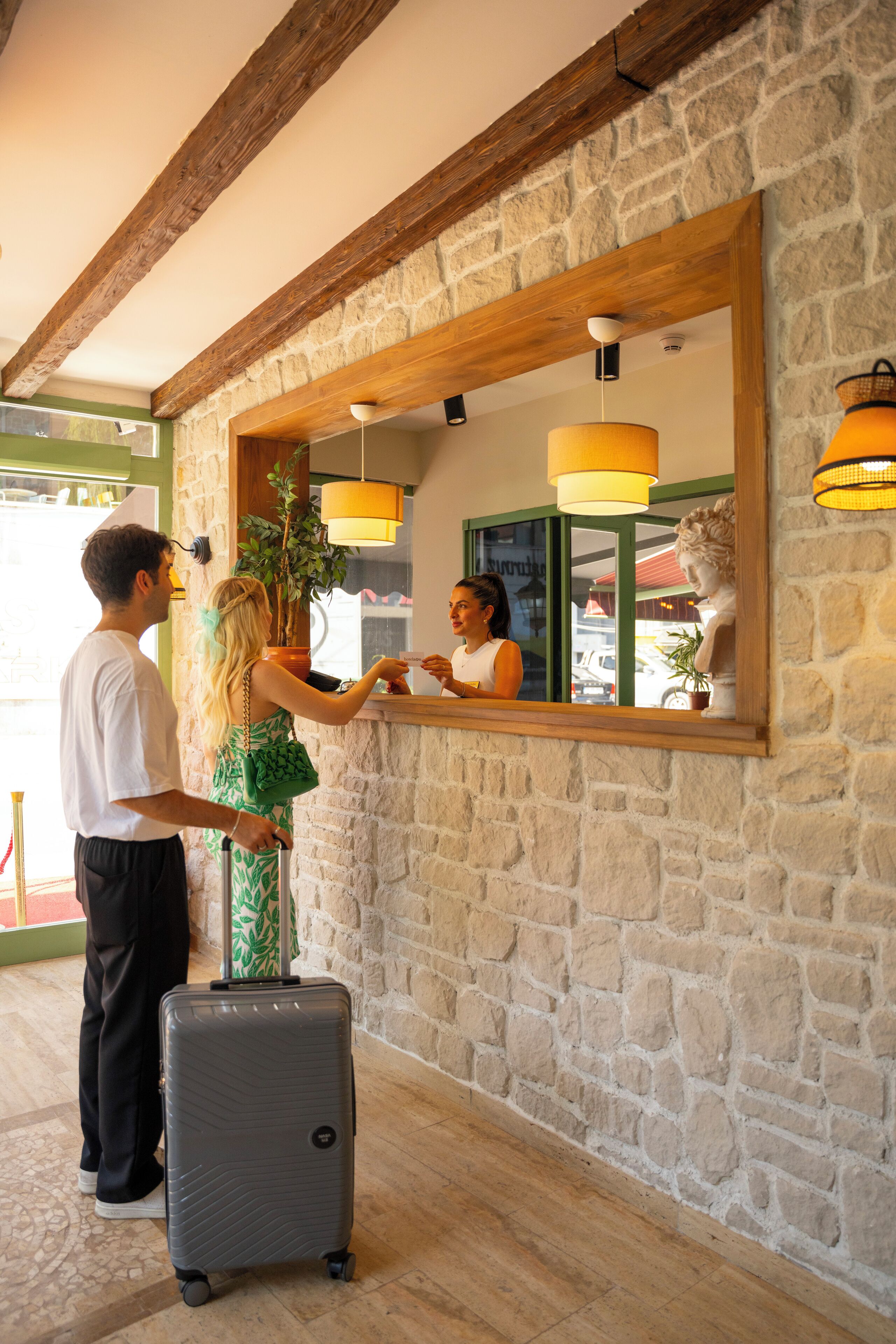 A reception area with a stone wall, wooden beams, and a large mirror reflecting a statue and a plant.