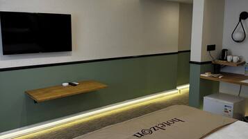 Habitación de hotel con cama, televisor montado, equipo de aire acondicionado, mesita de noche con una taza y un control remoto, y teléfono fijo en la pared.