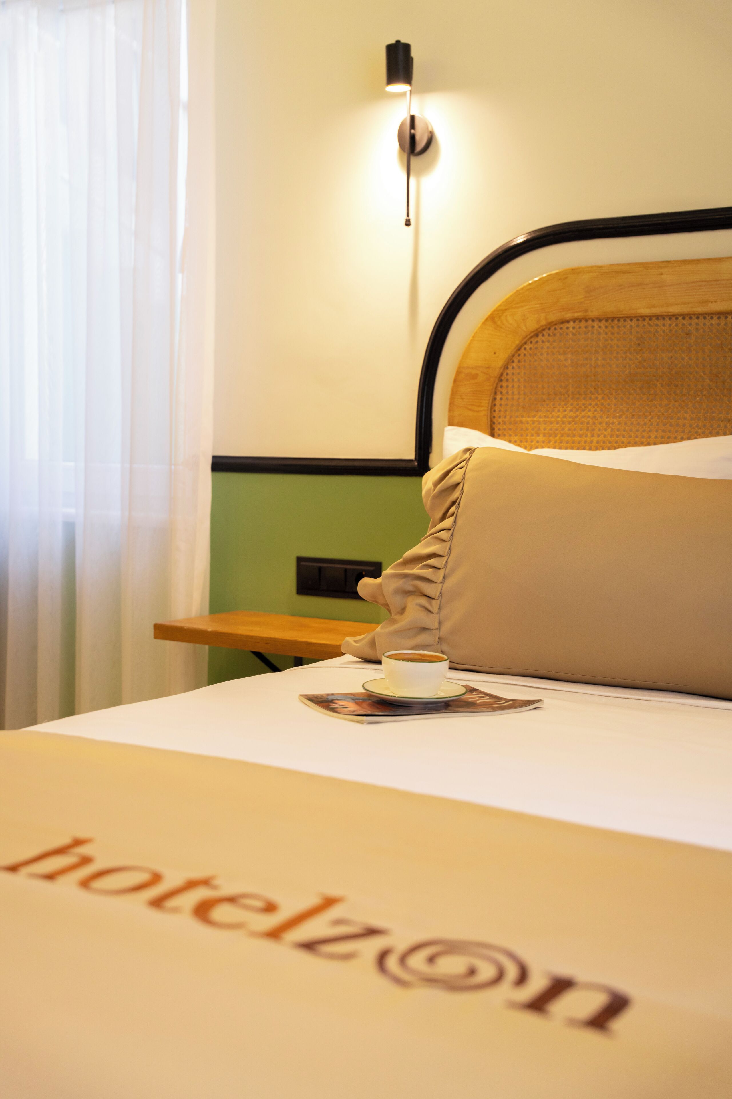 Habitación de hotel con cama, mesita de noche, lámpara y ventana con cortinas.