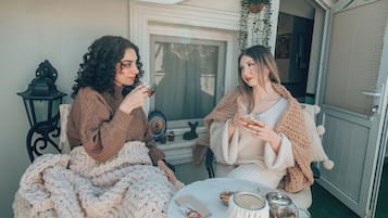 Dos personas sentadas en sillas afuera de un edificio, sosteniendo bebidas, con una mesa frente a ellas.
