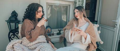 Dos personas sentadas en sillas afuera de un edificio, sosteniendo bebidas, con una mesa frente a ellas.