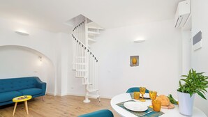A modern living room with a spiral staircase, a blue sofa, a dining table set with yellow glasses, and a potted plant. - Lily ancient stone mansion dating back to the 1400s (Volastra)