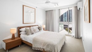 Un dormitorio moderno con una cama grande, un ventilador de techo y vistas a un paisaje urbano por la ventana.