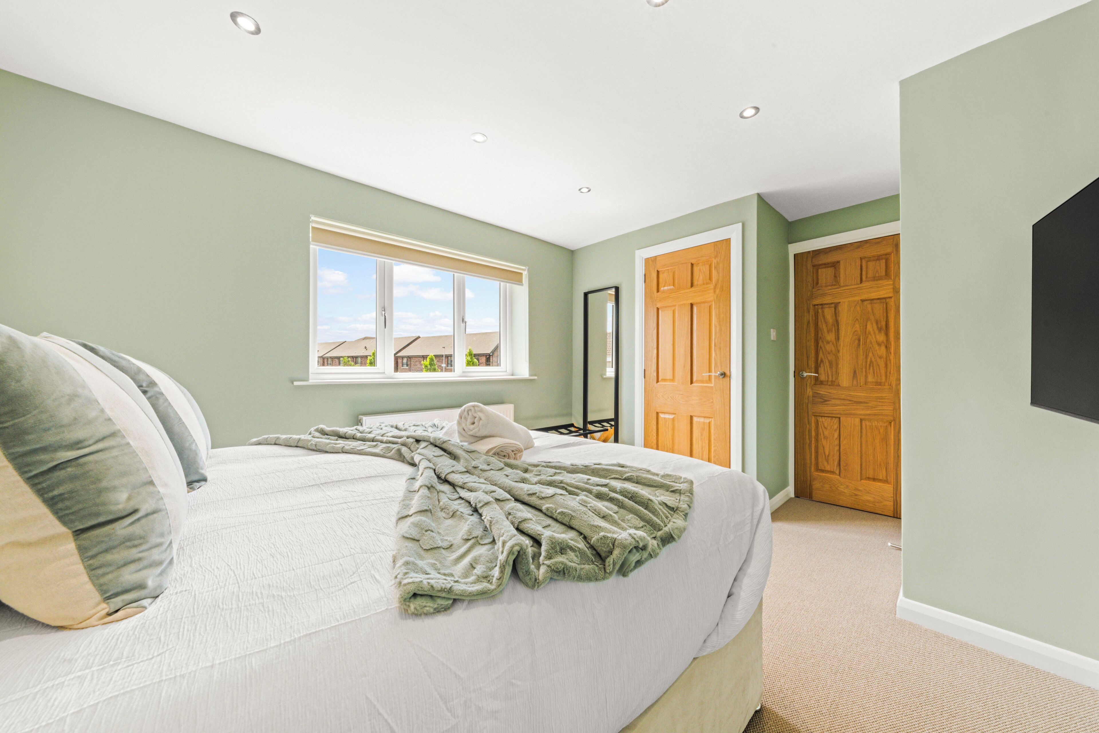 Een slaapkamer met een groot bed, een raam, een houten deur en een spiegel.