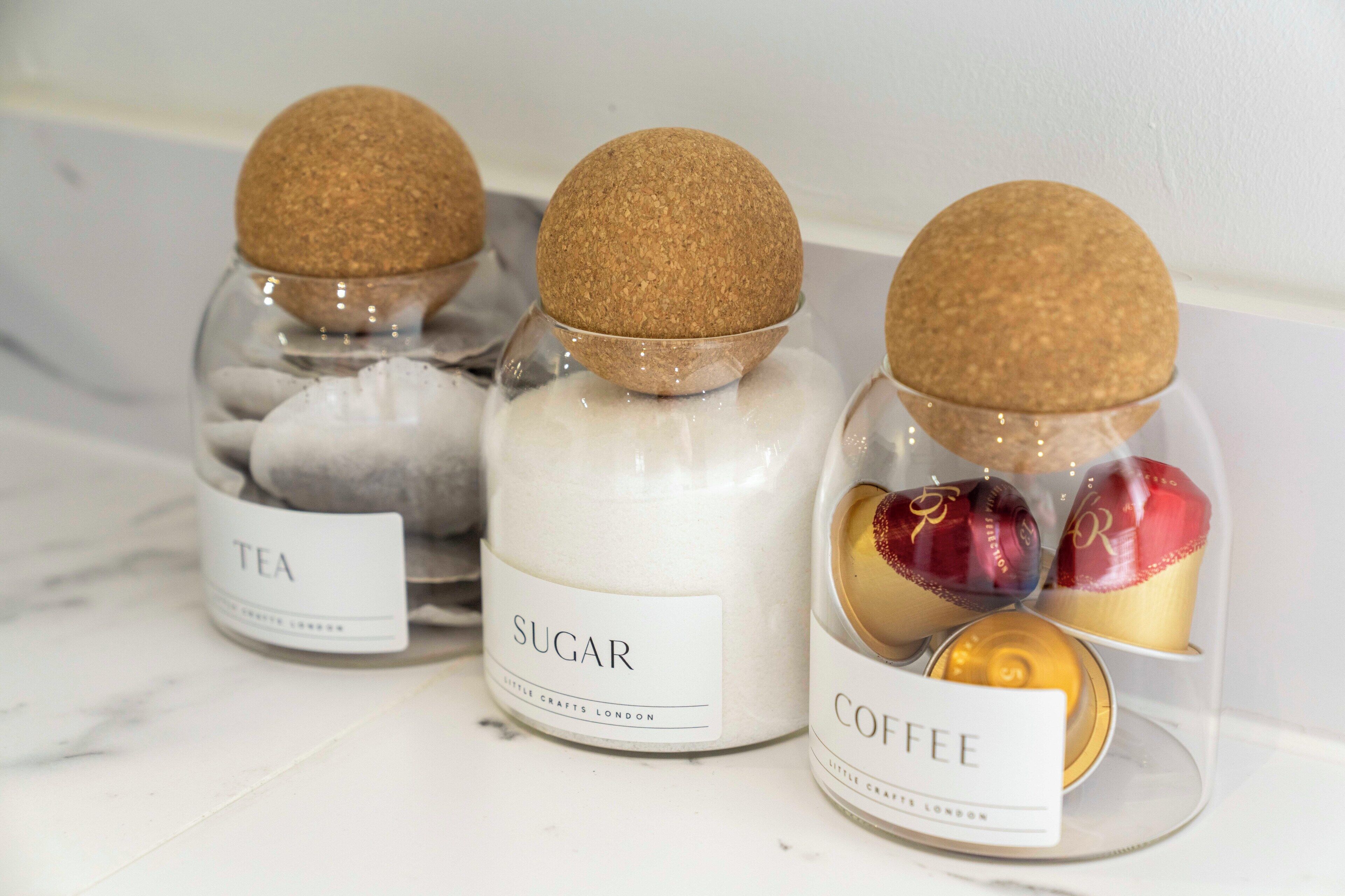 Three glass jars with cork lids, each labeled with a different scented product: tea, sugar, and coffee.