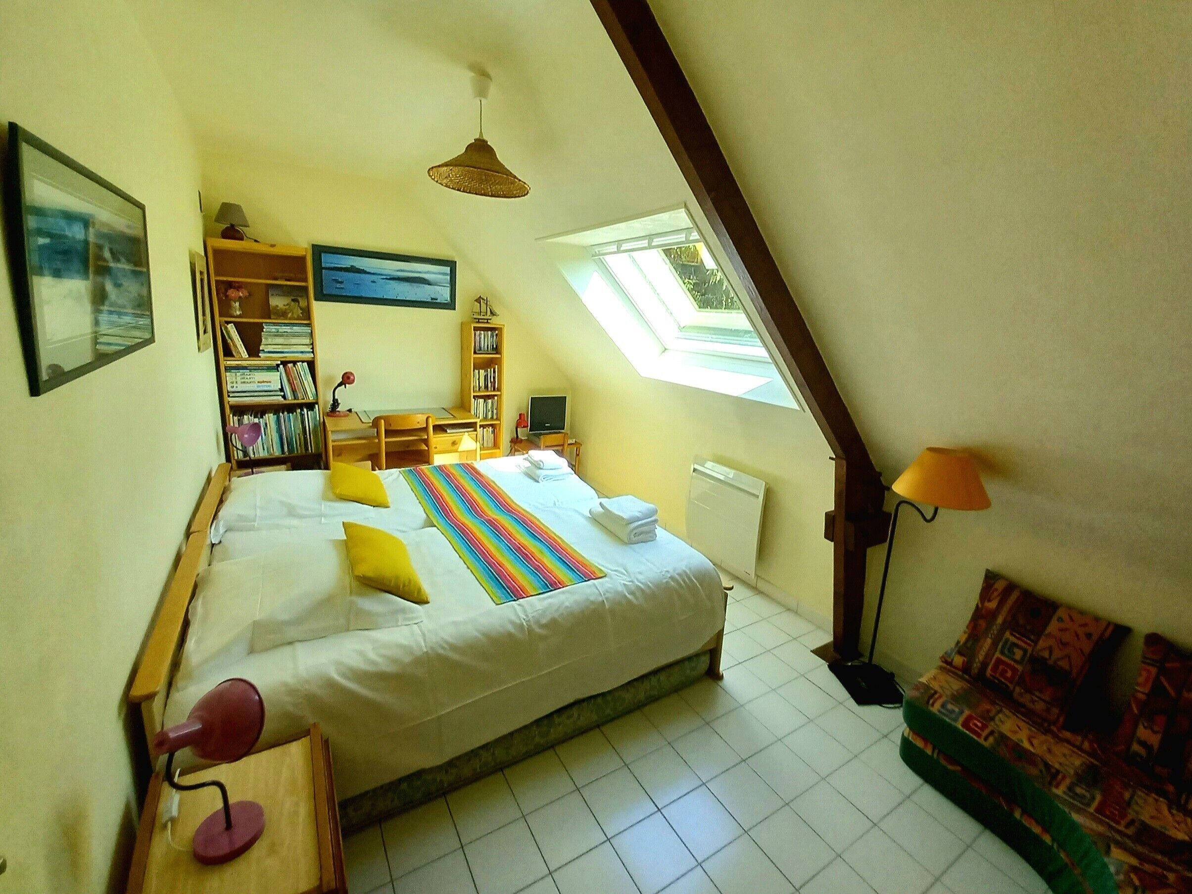 Une chambre à coucher avec un lit, un bureau, une bibliothèque, une télévision et une fenêtre.