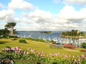 A marina with boats, a grassy area with flowers, and a distant island with a building.
