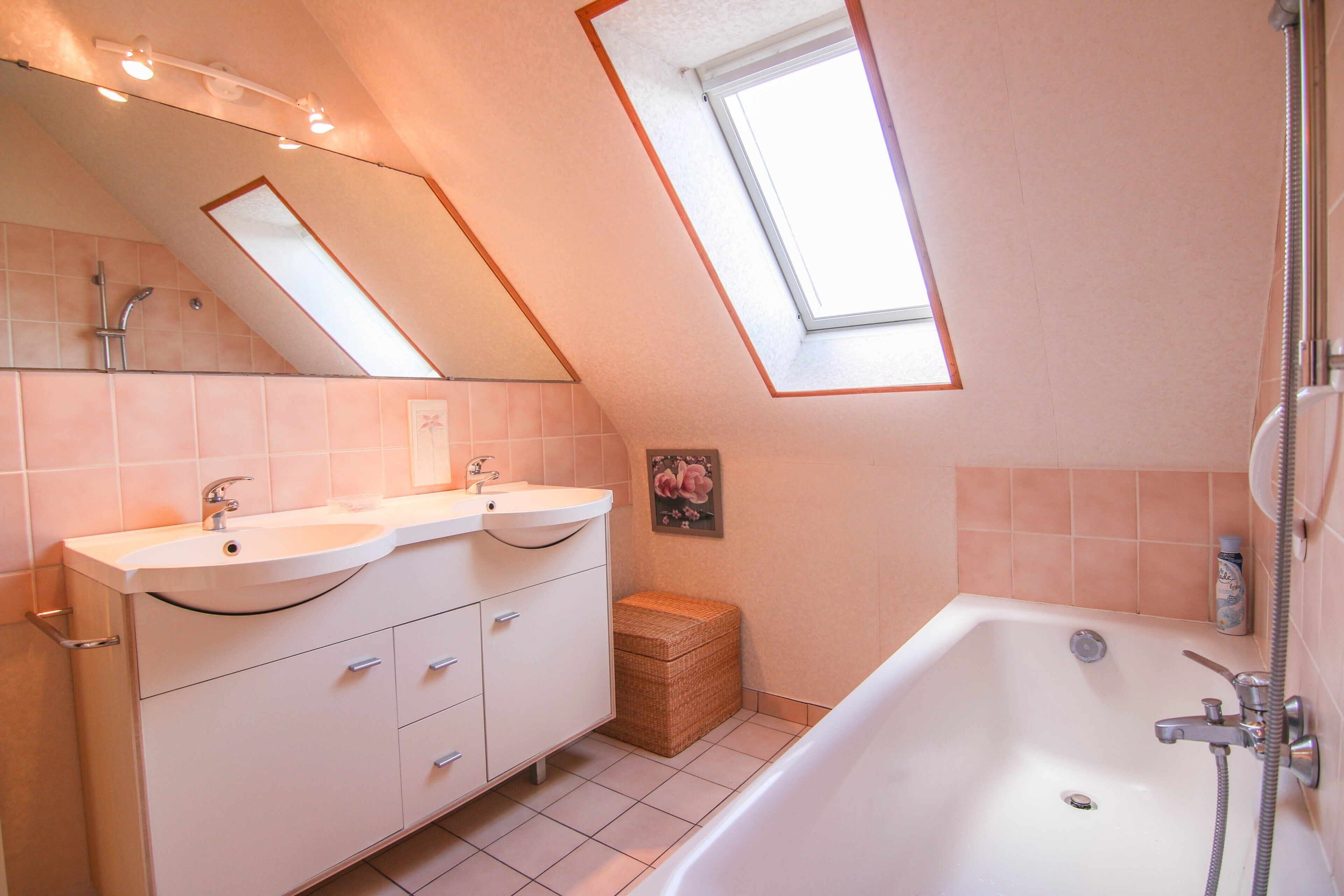 A bathroom with a skylight, a bathtub, a double sink vanity, and a small wicker basket.