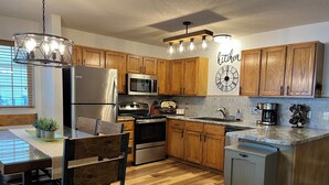 Una cocina moderna con armarios de madera, electrodomésticos de acero inoxidable, un comedor con mesa y sillas de madera, y un reloj decorativo en la pared.