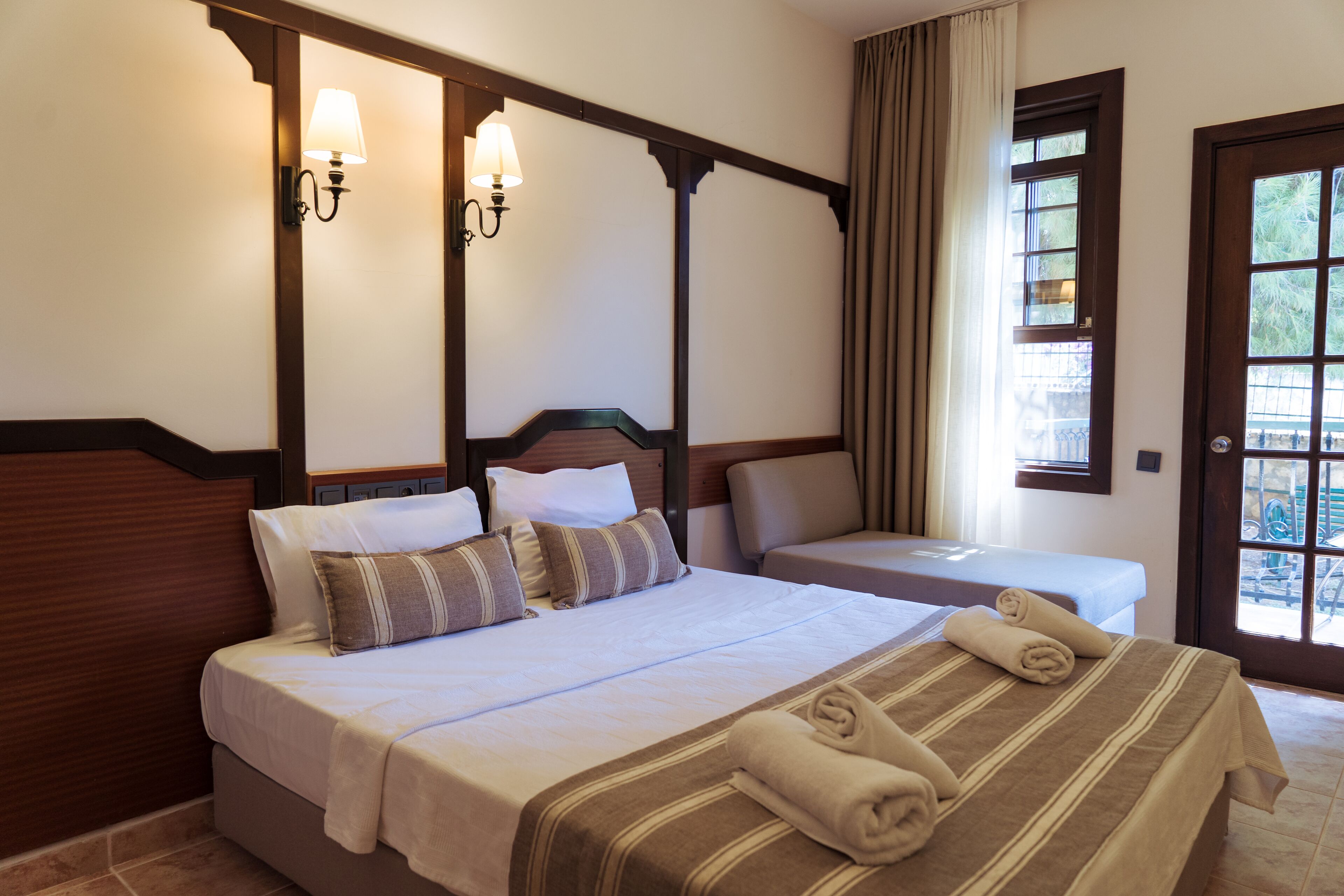 Habitación de hotel con una cama grande, una cama más pequeña y una ventana con cortinas.