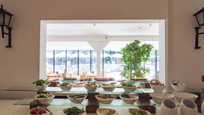 Un bufé con diversos platos y cuencos sobre estantes de vidrio, una planta en maceta y vista a un edificio con fachada de cristal.