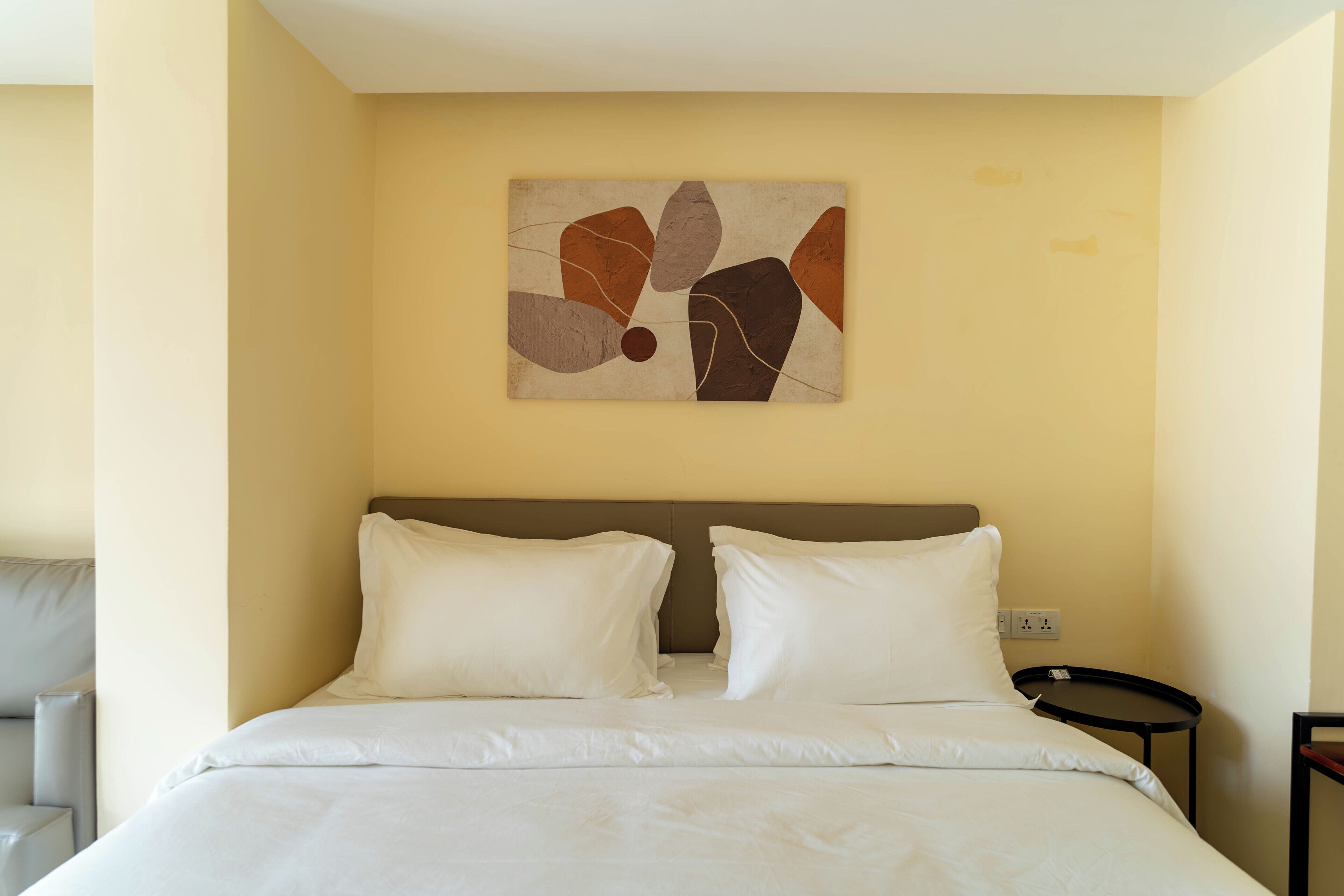 A hotel room with a bed, two pillows, a nightstand, and a wall art piece.