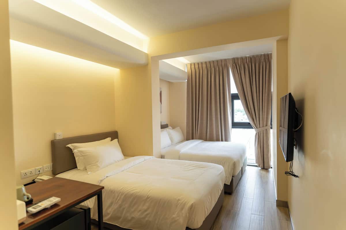 Une chambre d’hôtel avec deux lits, un bureau avec un téléphone et un téléviseur fixé au mur.