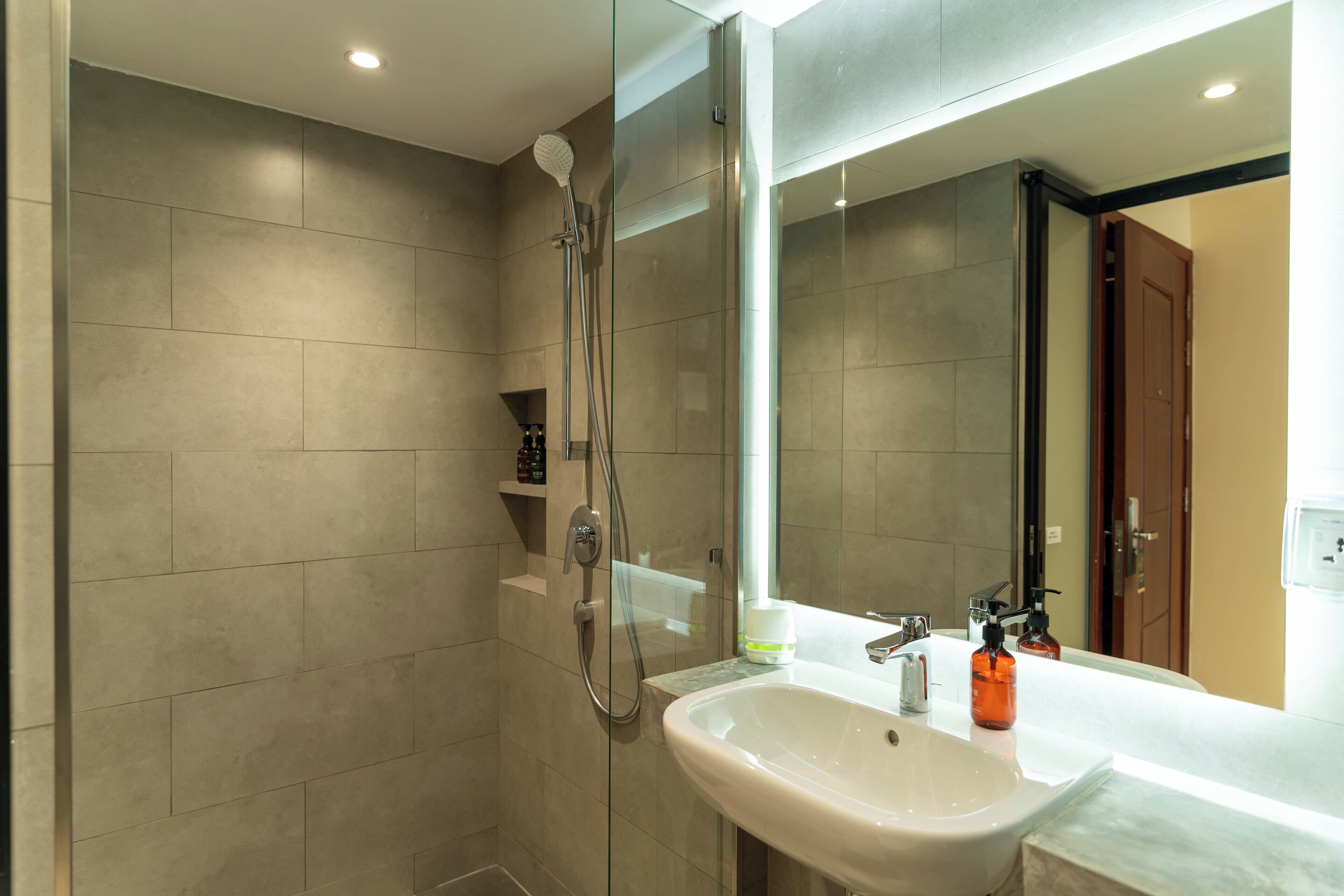 Une salle de bain moderne avec une douche à parois de verre, un lavabo blanc et un grand miroir.