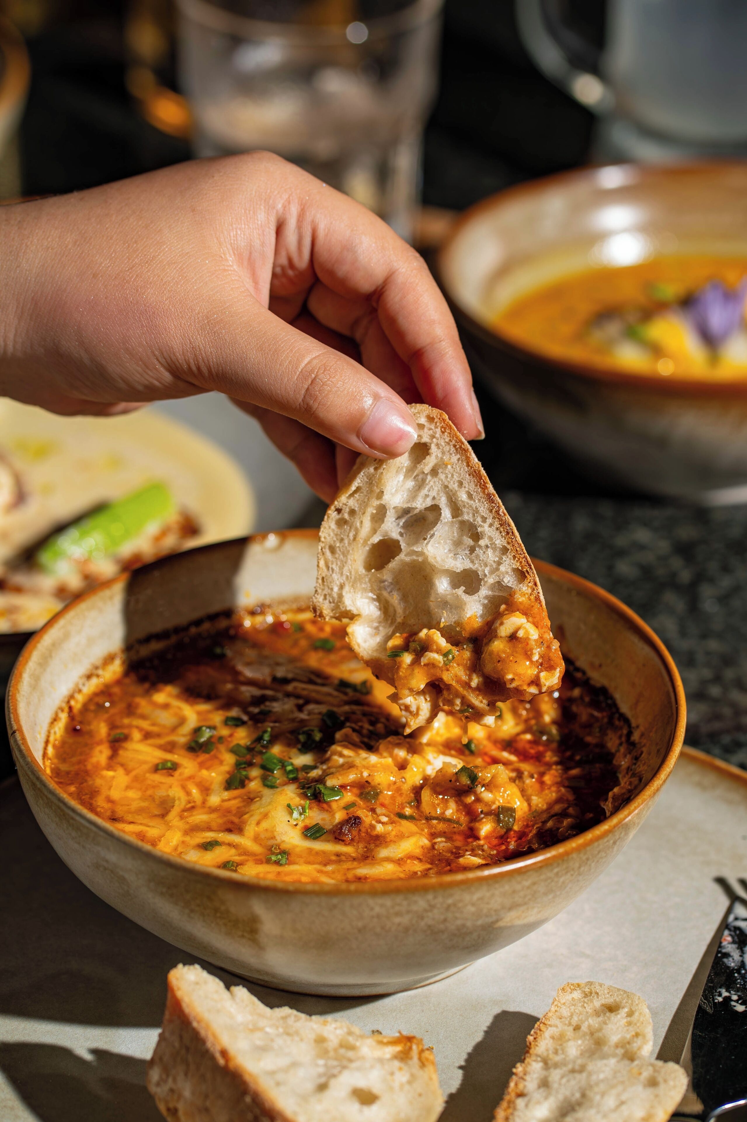 A hand dipping a piece of bread into a bowl of soup.