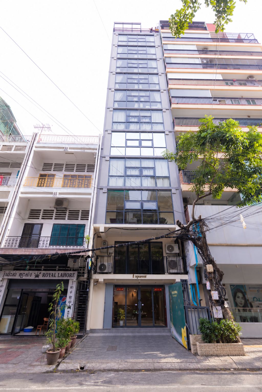 Un edificio de varios pisos con entrada a nivel de calle, balcones y un árbol en frente.